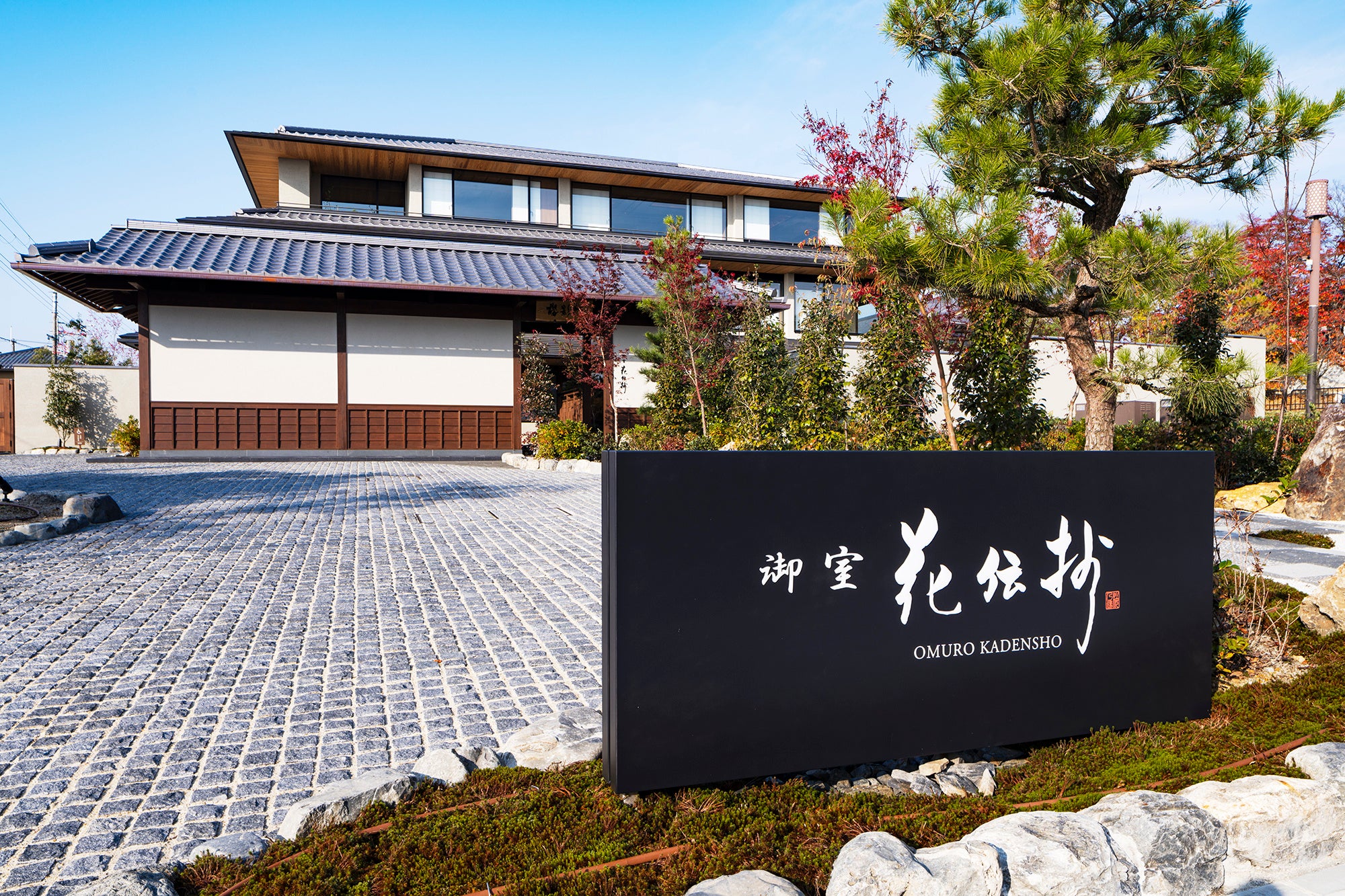 A modern Japanese hot-spring inn building with traditional architectural elements, set against a lush green landscape.
