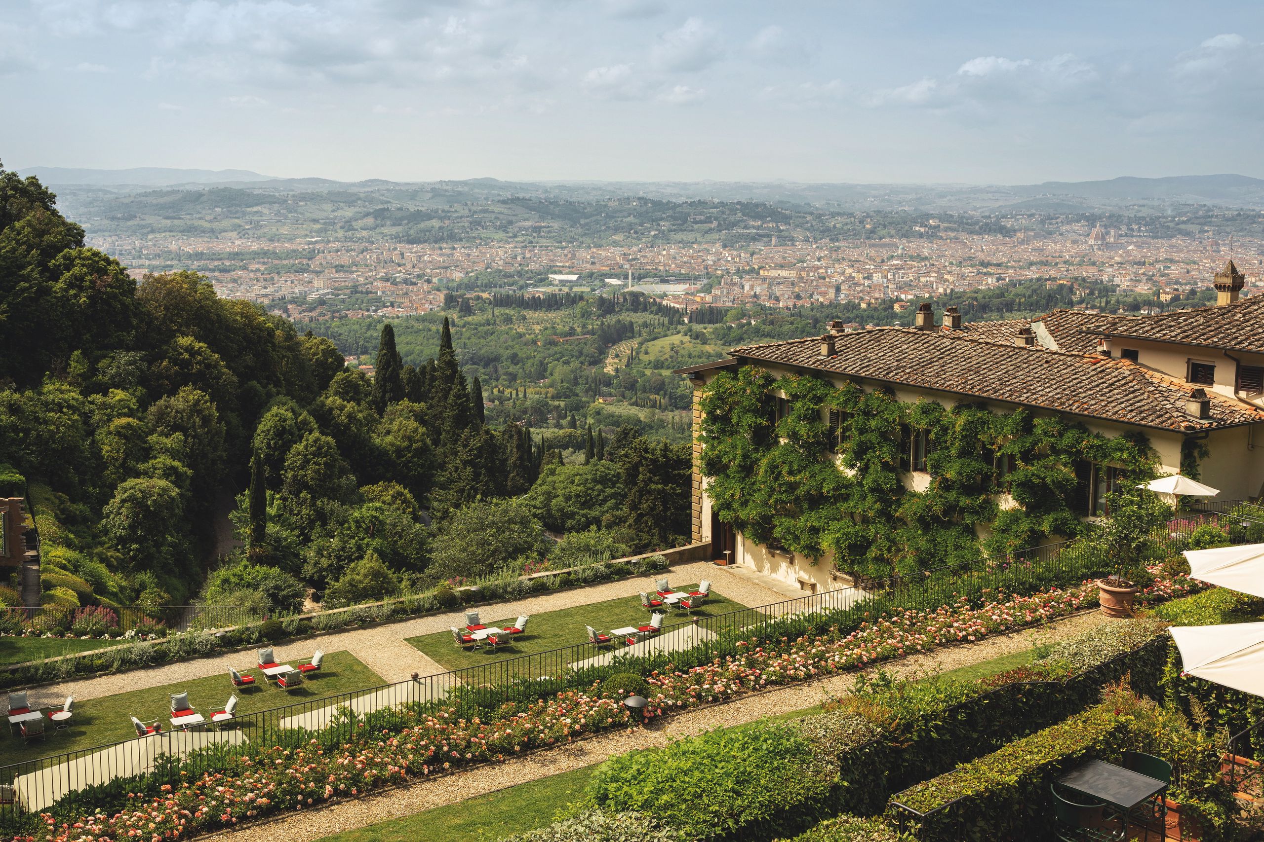 Exterior view of Villa San Michele, a historic building on a hillside overlooking Florence, with lush gardens in the foreground.