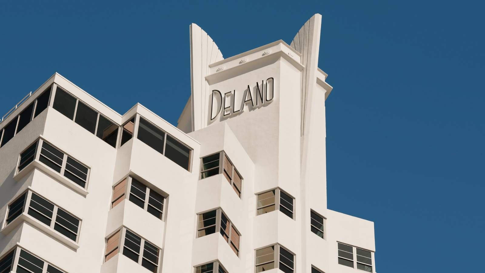 Exterior view of the Delano Miami Beach hotel, showcasing its white Art Deco architecture and prominent signage against a clear sky.