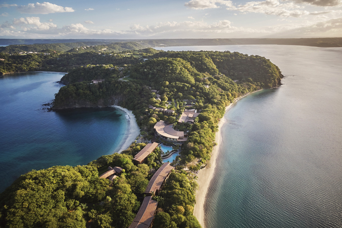 Aerial view of a luxury resort nestled into a lush, green peninsula with ocean on two sides, showcasing integration with nature.