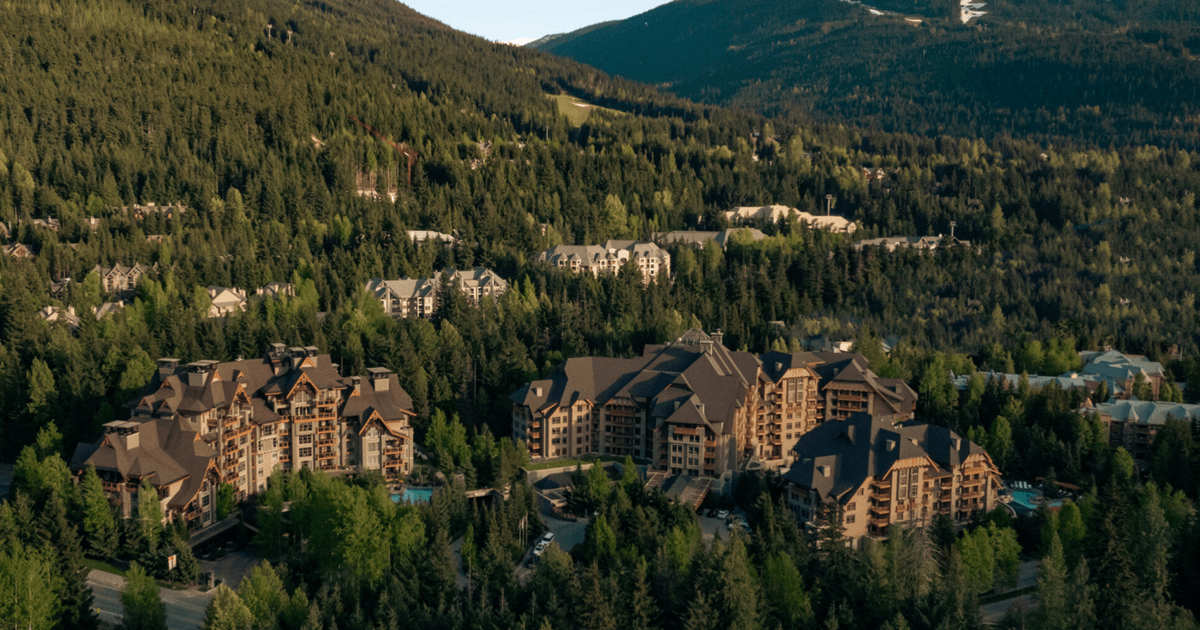 A modern, warm-toned hotel lobby with a large fireplace, plush seating, and an expansive window view of snow-capped trees.