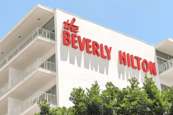 An architectural rendering of the One Beverly Hills development, featuring sleek modern towers surrounded by lush, expansive gardens and reflective water features under a clear sky.