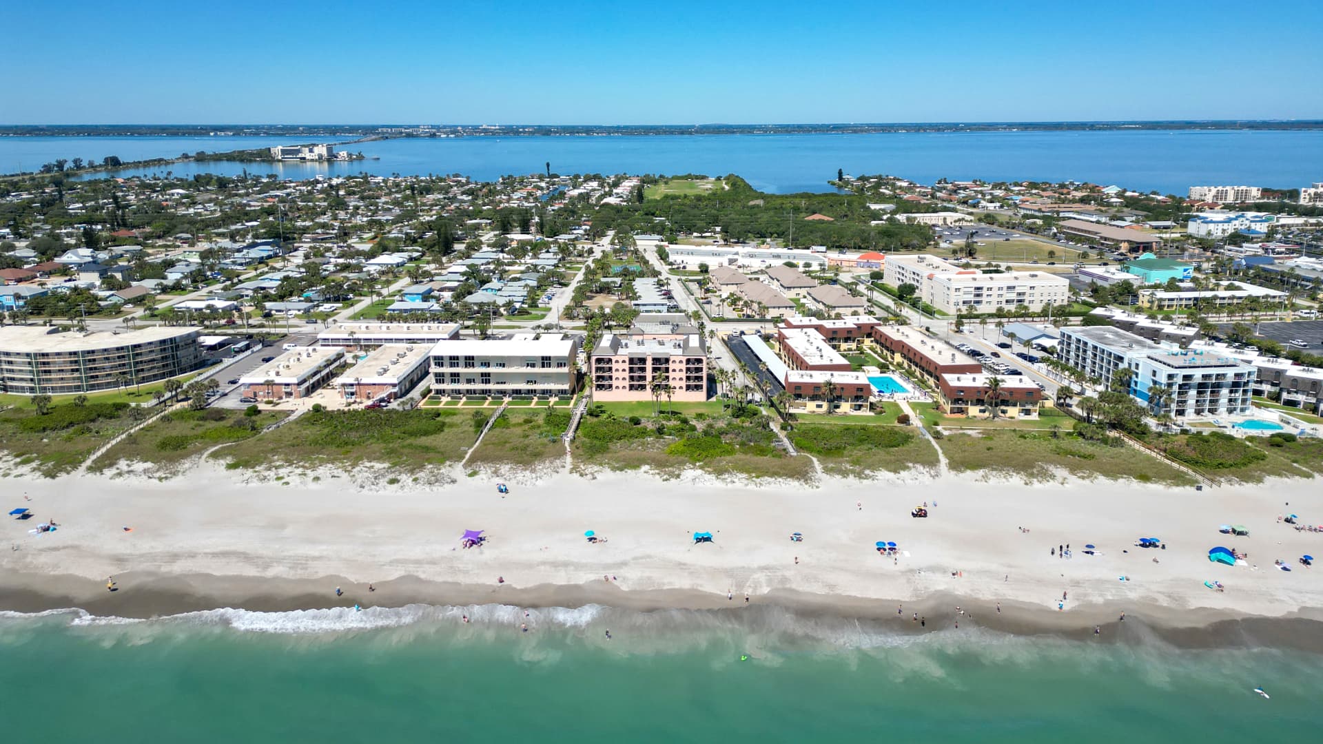 A sleek, modern luxury hotel overlooking a Florida beach, with a rocket launching in the distance