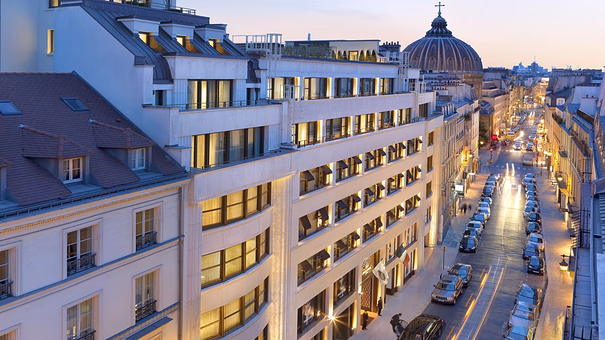 Exterior view of a grand luxury hotel in Paris at dusk, with lights illuminating the facade