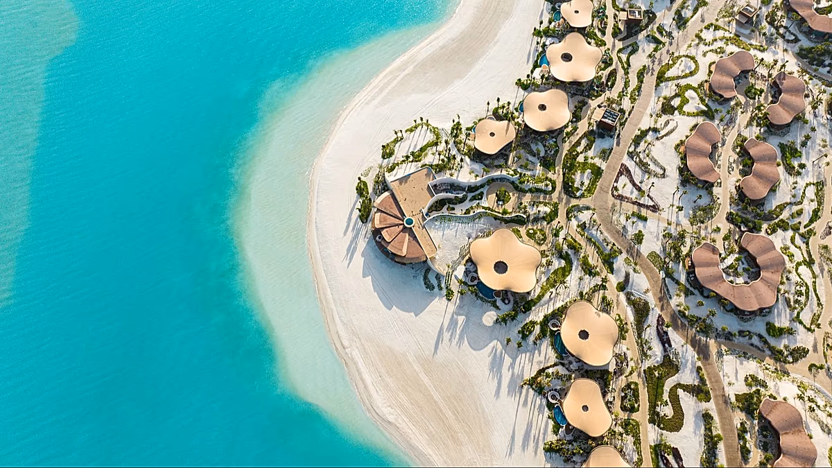 Aerial view of a luxury resort with swimming pools and a long beach along a turquoise sea