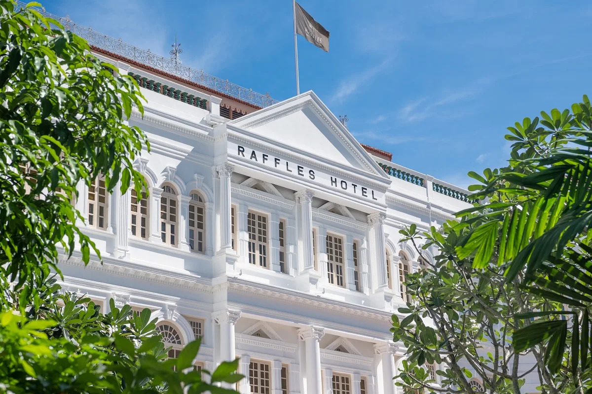 The white colonial facade of Raffles Hotel Singapore, framed by lush tropical greenery