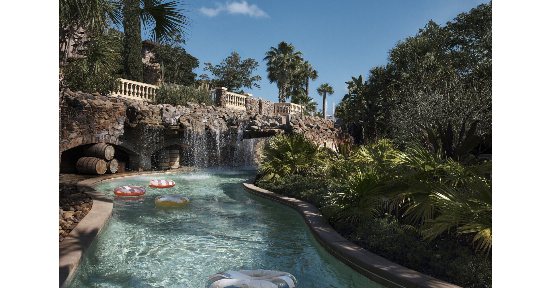 Aerial view of a sprawling resort waterpark featuring a lazy river, water slides, and multiple pools, surrounded by lush landscaping.