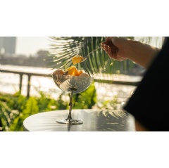 A vibrant riverside scene at the Four Seasons Hotel Bangkok, featuring an elegant ice cream bar with customers enjoying treats by the Chao Phraya River.
