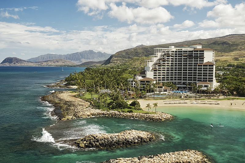A resort pool and oceanfront property on a tropical island with palm trees under a blue sky.