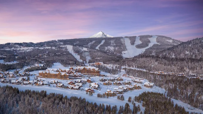 Aerial view of Montage Big Sky resort in winter, nestled among snow-covered mountains with lights illuminating the property.