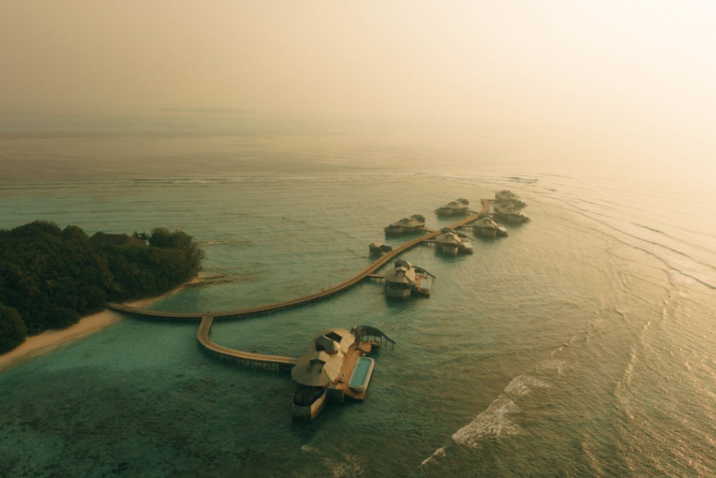 An aerial view of a luxurious Soneva resort in the Maldives, showing overwater villas and pristine turquoise waters.