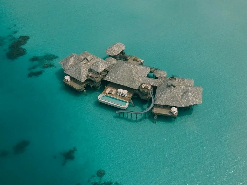 An aerial view of a luxurious Soneva overwater villa at sunset, surrounded by turquoise water and lush tropical vegetation