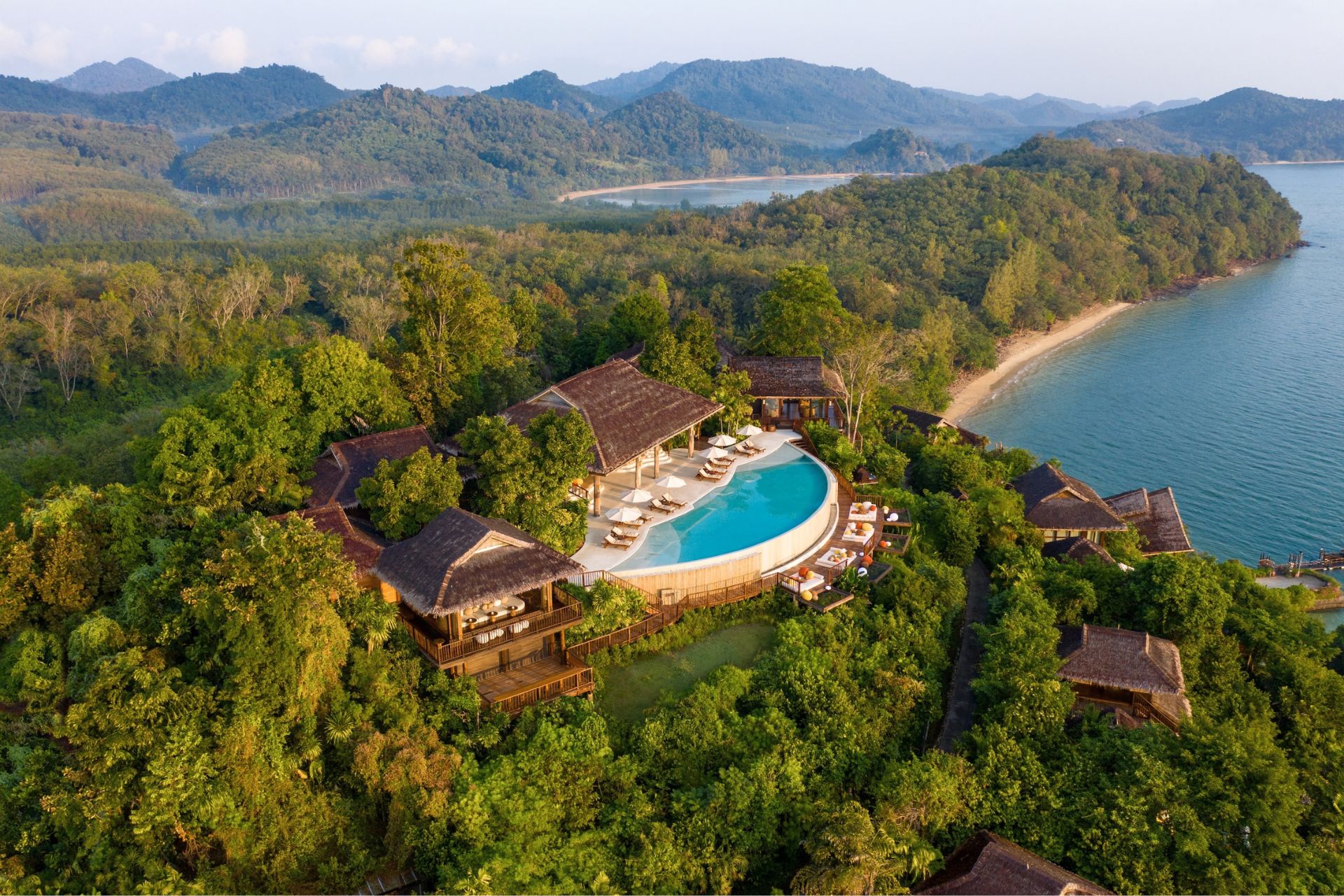 Aerial view of Six Senses Yao Noi resort villas nestled amongst lush greenery overlooking a serene bay with limestone karsts