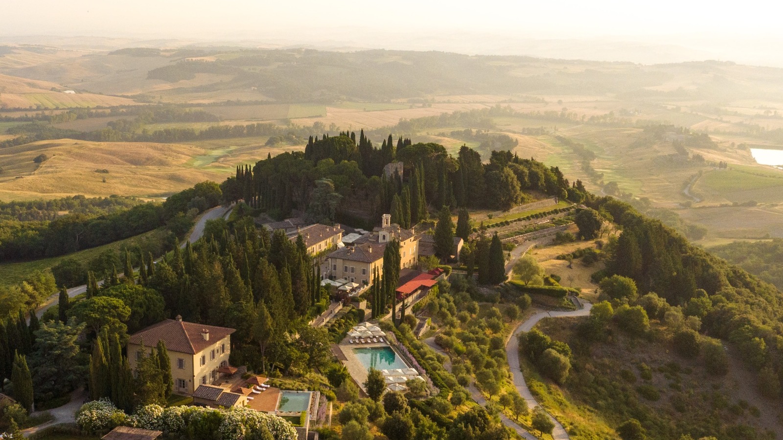 Aerial view of Castiglion del Bosco, A Rosewood Hotel, showing vineyards and historic buildings at sunset