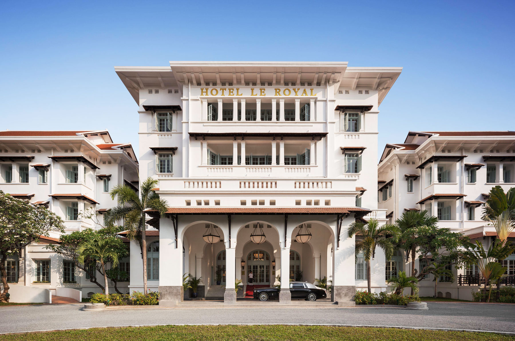 Exterior view of Raffles Hotel Le Royal, a grand colonial-style building with white facade and green awnings.
