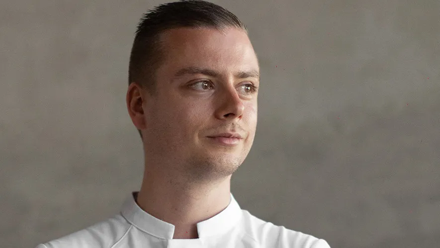 Evan Neumann, a man in a chef's jacket, smiling in a professional kitchen