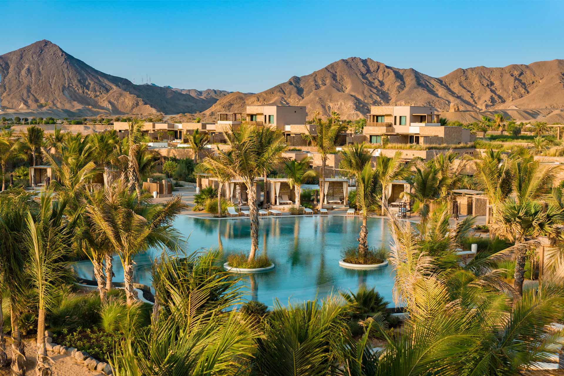 An aerial view of the Six Senses Amaala resort, showing modern architecture blending into a coastal desert landscape with swimming pools and palm trees.