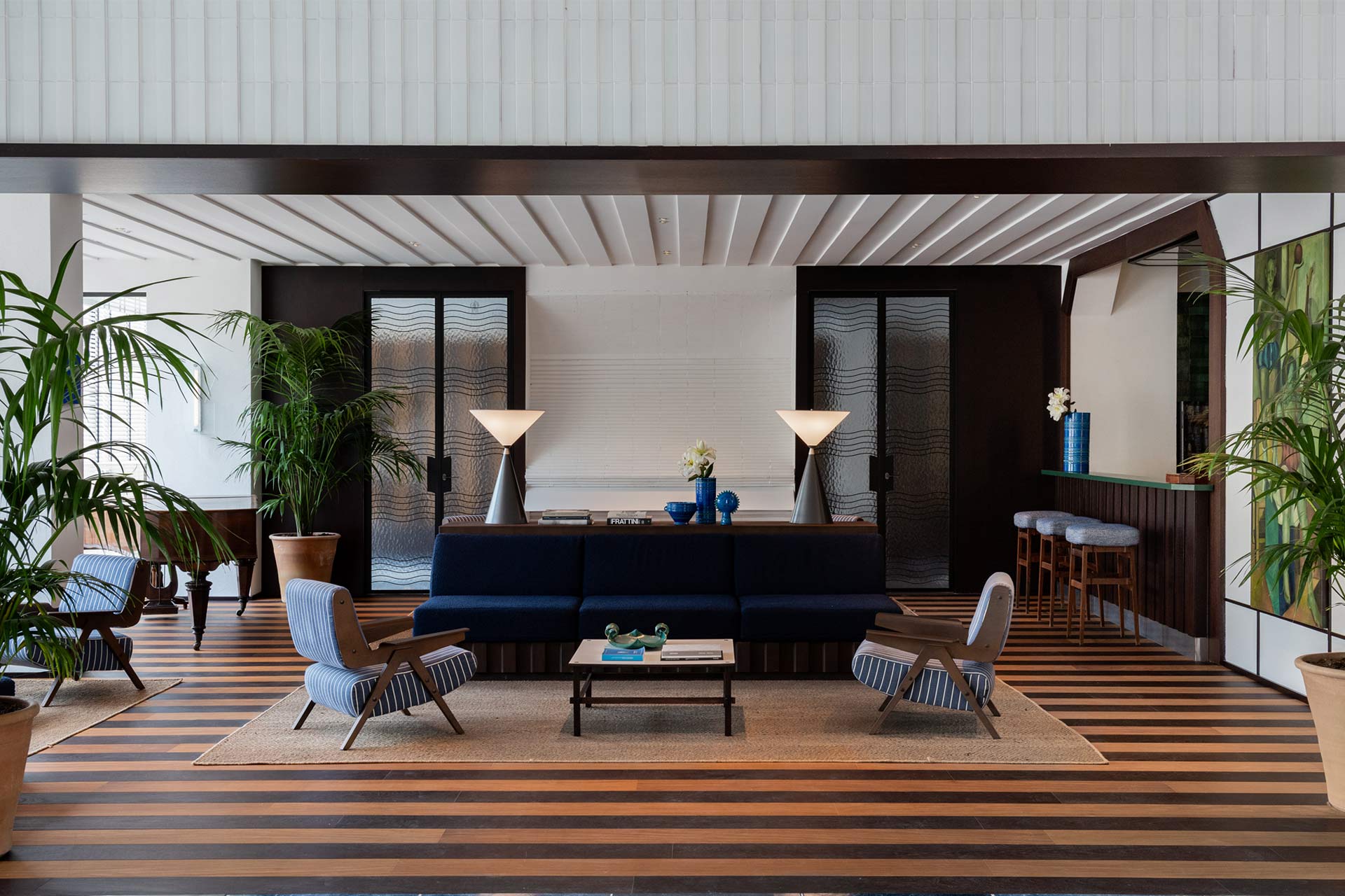 Luxueux lobby d'hôtel avec de hauts plafonds, de grandes fenêtres, une table octogonale en granit et des sols polis aux tons bleus, reflétant la lumière naturelle.