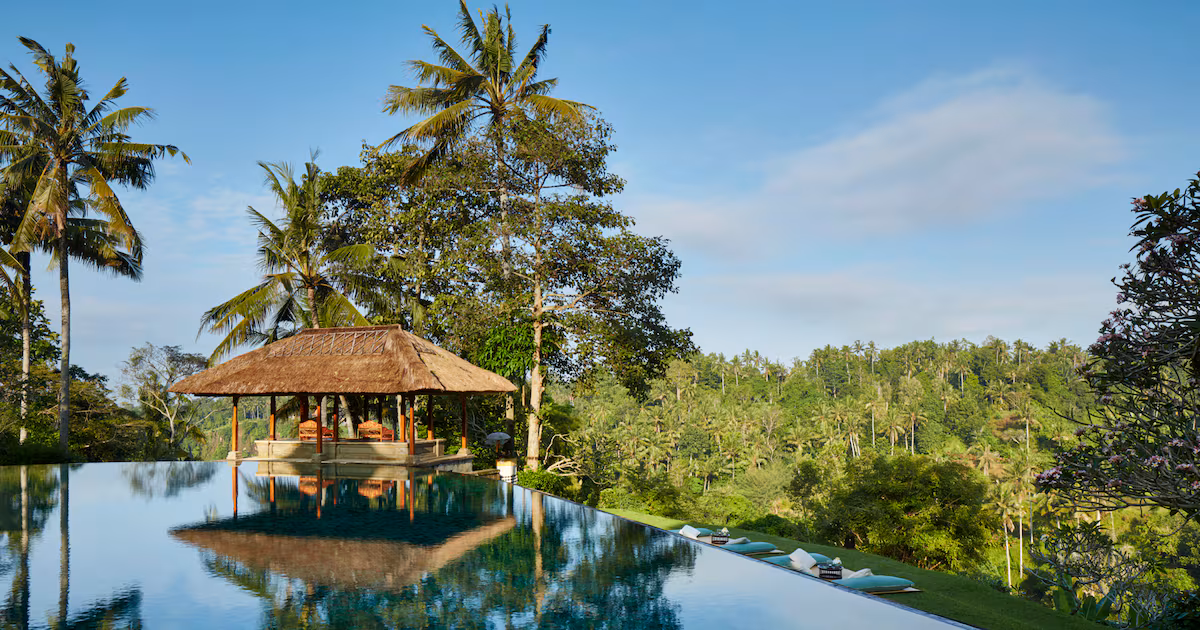 An aerial view of a luxury resort nestled within a lush green rainforest, with distant mountains and ocean visible.