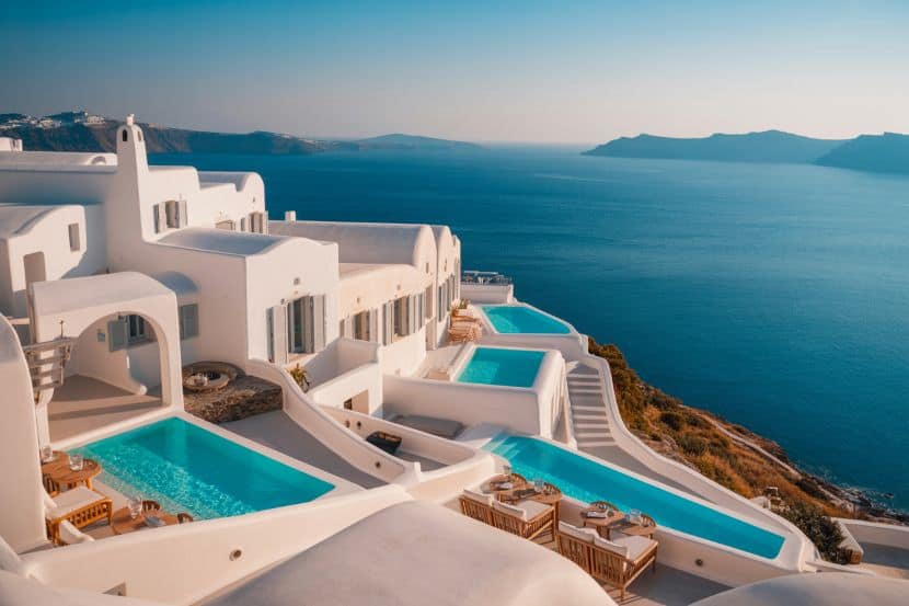 A sweeping view of the Four Seasons Hotel Mykonos, featuring whitewashed buildings cascading down a cliffside toward the Aegean Sea.