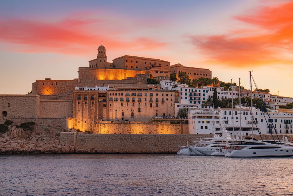 Panoramic view of Dalt Vila fortress in Ibiza, Spain, at sunset, with the Parador de Ibiza visible within its ancient walls overlooking the Mediterranean Sea